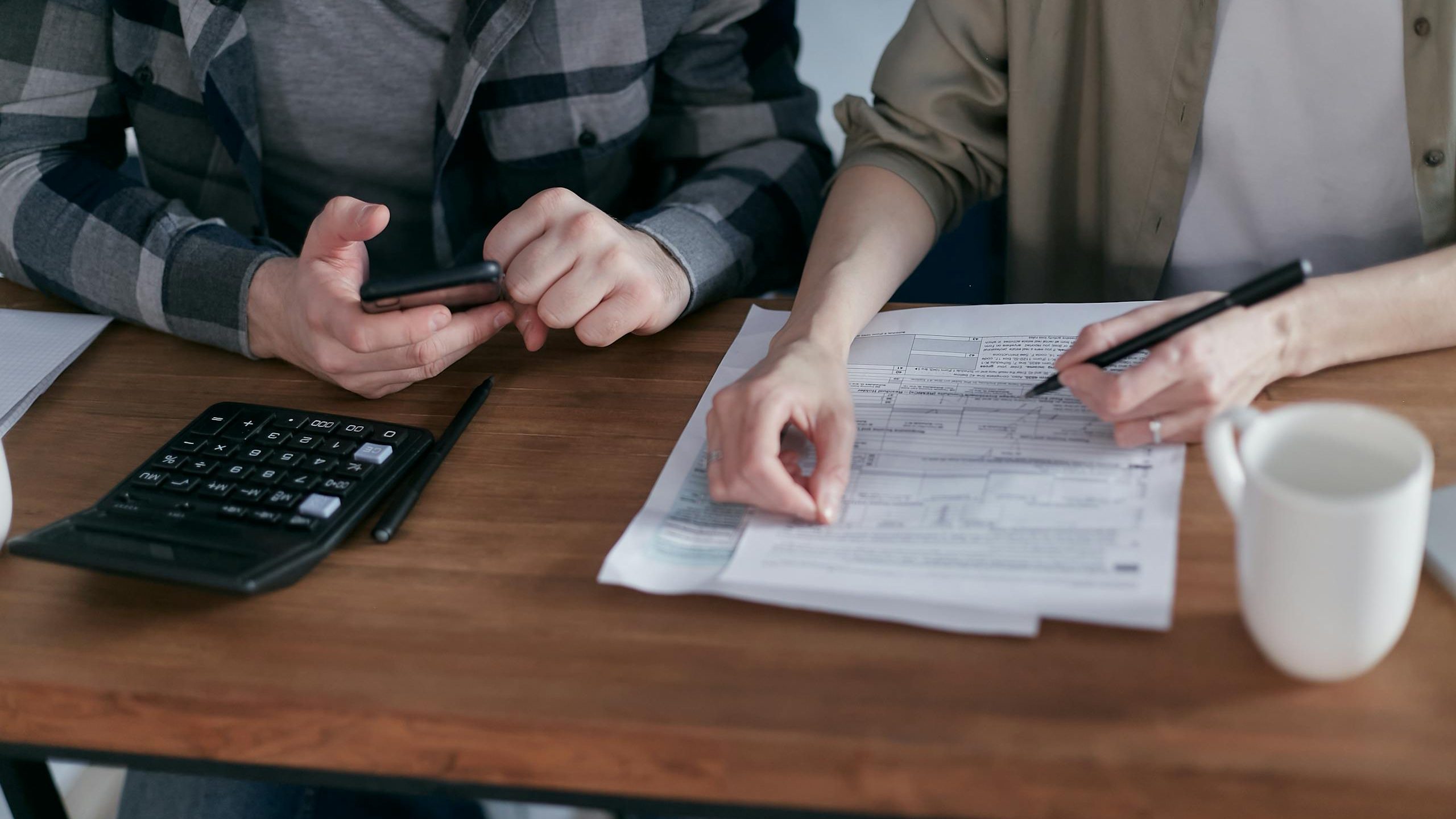 A couple diligently reviews their finances using a calculator and documents at home.