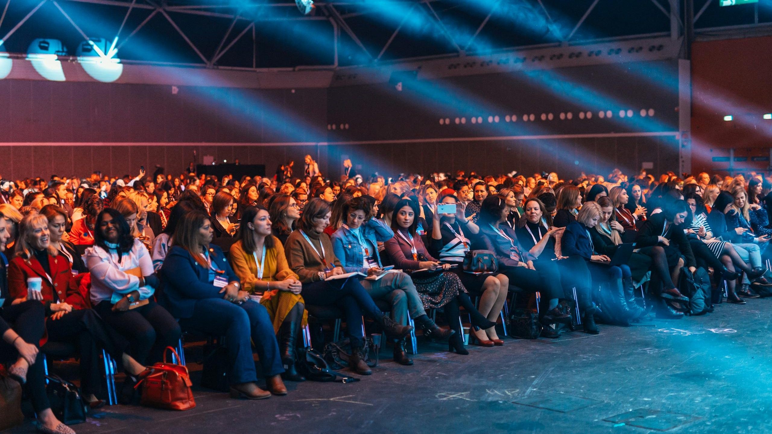 Vibrant image of a diverse audience seated in a large auditorium, highlighted by dynamic stage lighting.